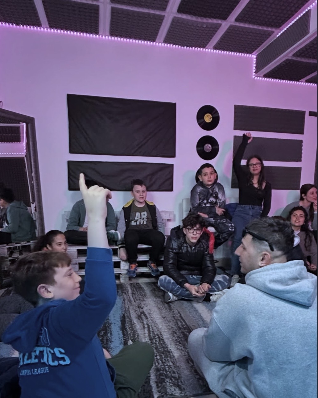 Partecipanti e operatori riuniti in cerchio durante un laboratorio musicale in studio.